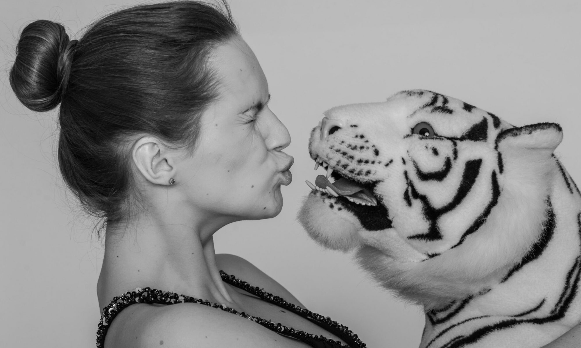 Humorvolle Studioaufnahme: Frau macht einen Kussmund zu einem weißen Plüsch-Tiger – verspielte Szene in Schwarz-Weiß.