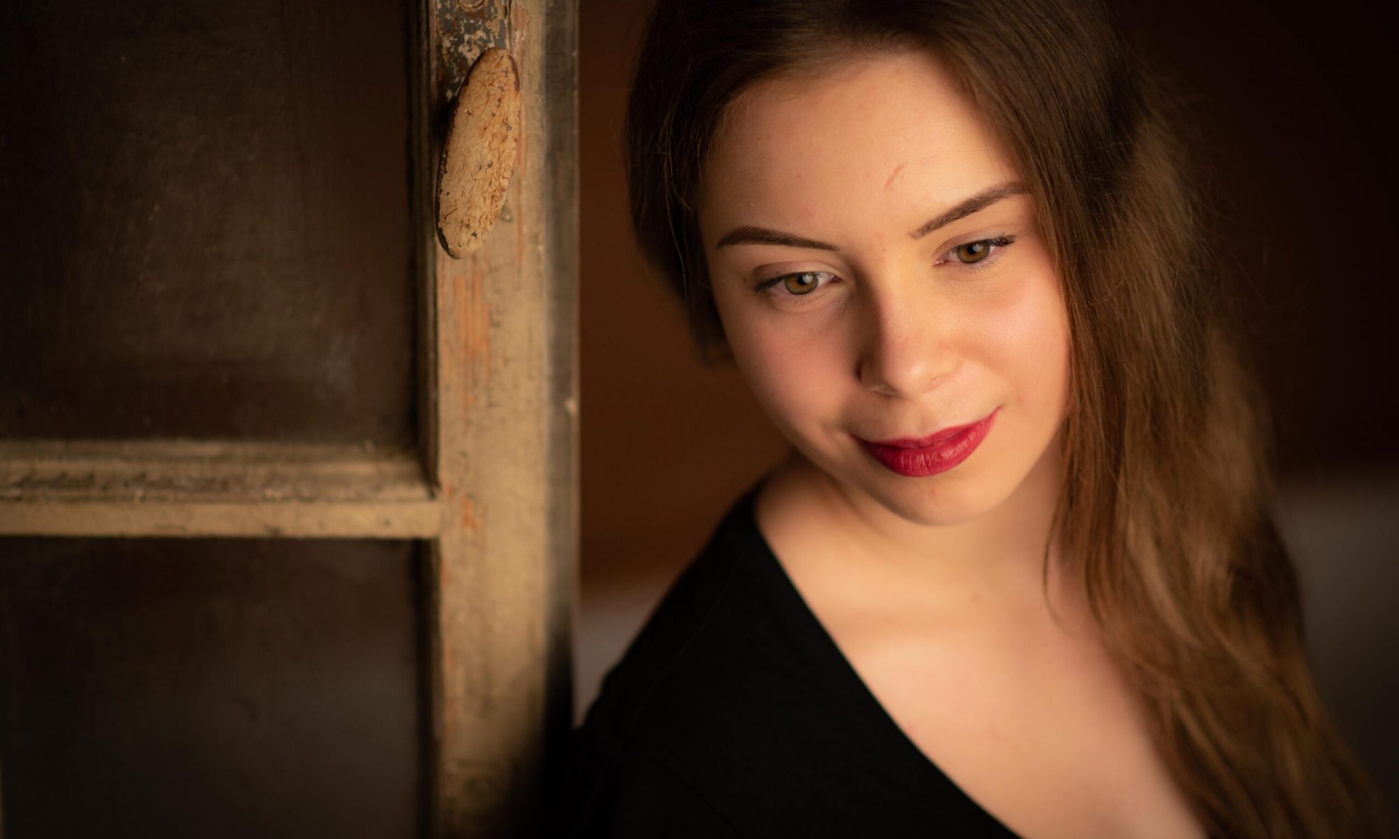 Porträt einer jungen Frau mit rotem Lippenstift am Fensterrahmen – warmes Licht und nostalgische Atmosphäre.