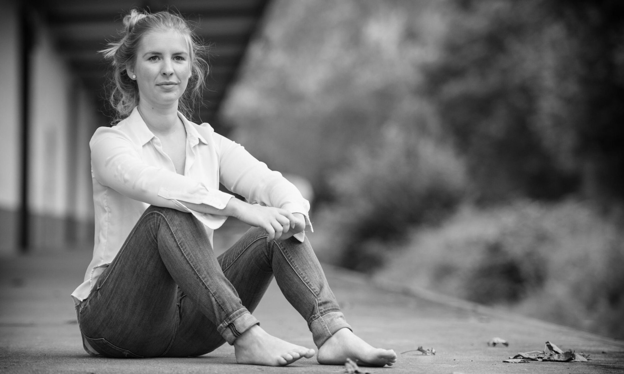 Frau sitzt Barfuß auf einem Bahnsteig, schwarz-weiß in Szene gesetzt.